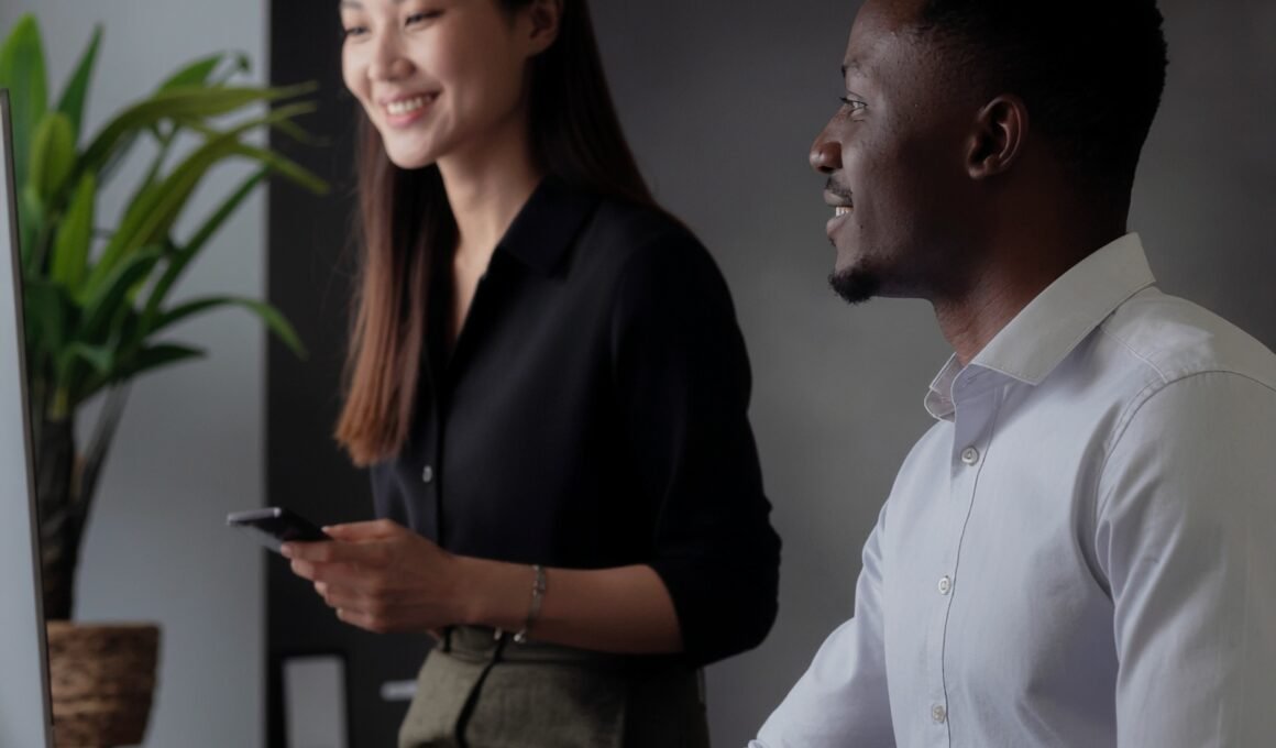 Young white female and black male looking at his computer screen - the mood is uplifting as if they’ve just discovered something positive.