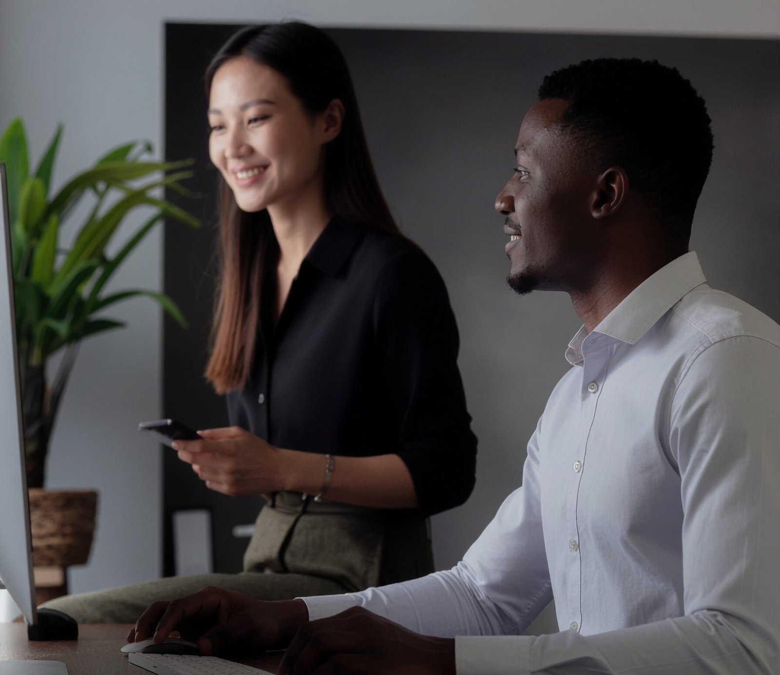 Young white female and black male looking at his computer screen - the mood is uplifting as if they’ve just discovered something positive.