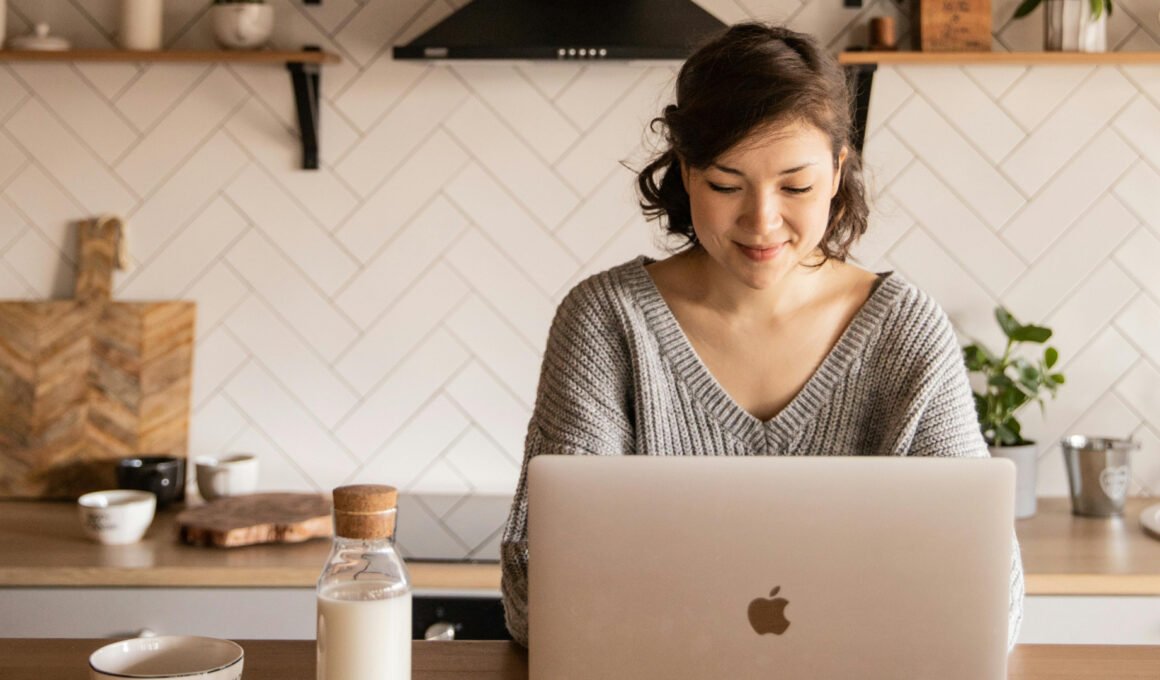 Asian female typing on a Macbook Air, sitting at a her kitchen. This feature image is about simple blog ideas for beginners
