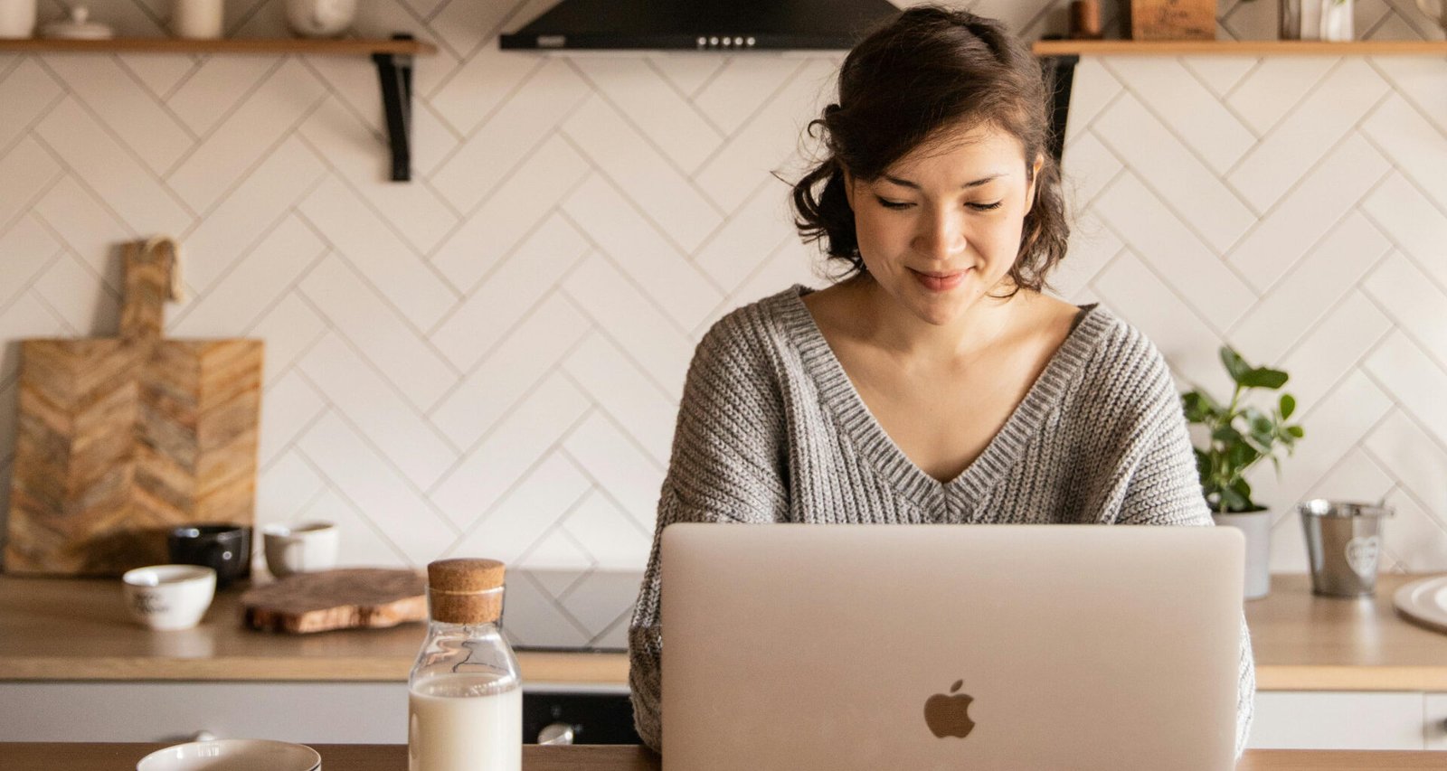 Asian female typing on a Macbook Air, sitting at a her kitchen. This feature image is about simple blog ideas for beginners