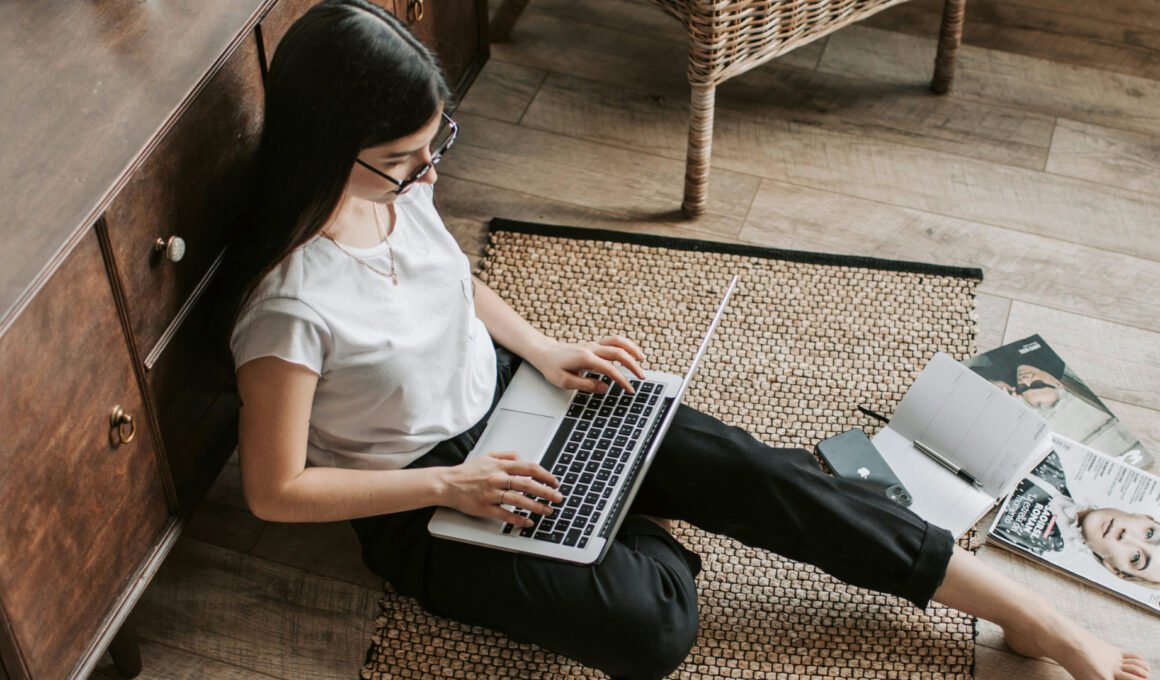 Feature image of a young white girl, sitting on the floor with a laptop of her lap, leaning against a cabinet, typing as if blogging. For the article: 'How to Come Up With Blog Post Ideas That Actually Get Traffic'/