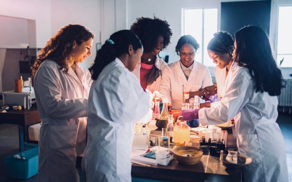 Image of multiracial women in a laboratory in lab coats experimenting with formulas denoting experimenting with cooking and food content for the article 'How to Start a Profitable Recipe Blog in 2026 (The Stack I’d Actually Use)'