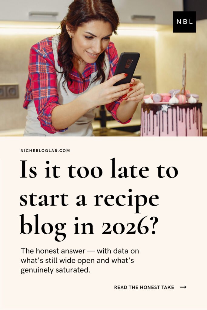 A pinterest pin graphic on cream colour background - half the image is a photo of a smiling female content creator photographing her cake creation with a smart phone. It represents the article "How to Start a Profitable Recipe Blog in 2026". The headline on the pin is: 'Is It Too Late to Start a Recipe Blog in 2026?'.