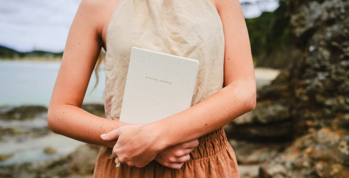 Woman holding her journal in her hands with tranquil seaside in the background. How to start bullet journalling - for beginners.