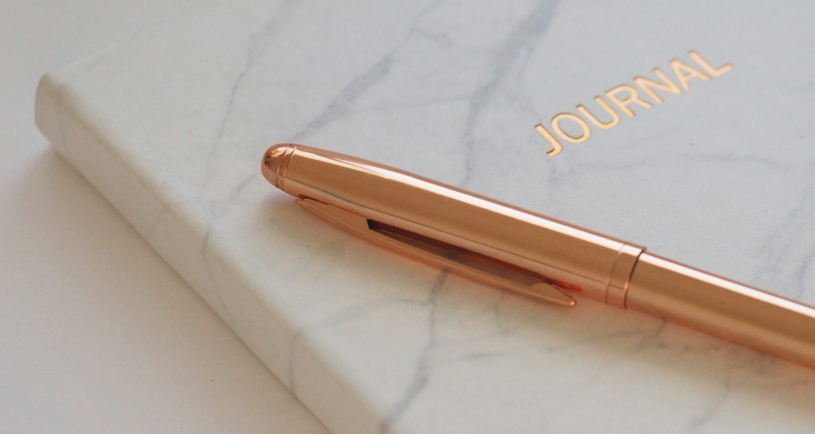A marble patterned journal with gold title and pen on a white table. Starting a bullet journalling practice.